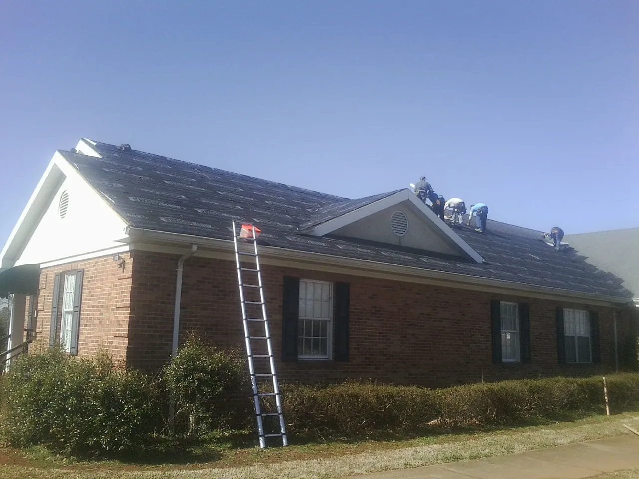 Crew tearing shingles off a brick ranch roof with a ladder set — Emergency Roof Repair work by our crew in West Salisbury