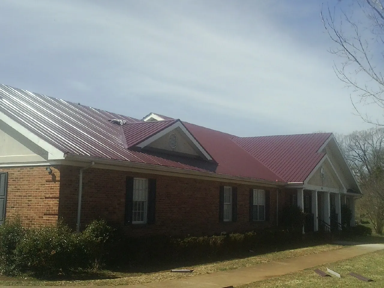 Red metal roof with gabled entries on a long brick building, from a Hail Damage Roof Repair job in West Salisbury