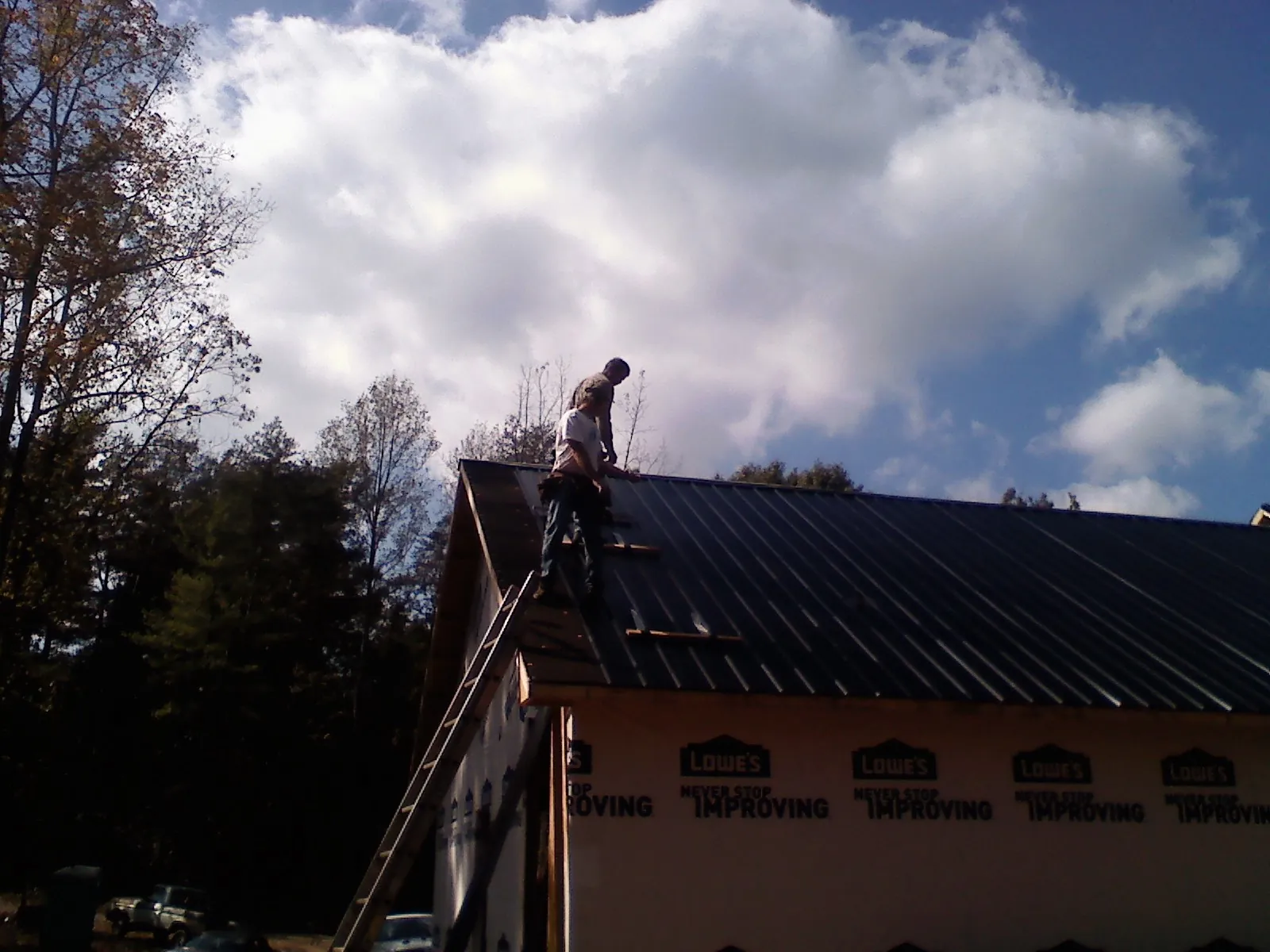 Roofer fastening dark metal panels high against a cloudy sky, from a Roof Inspection job in West Salisbury