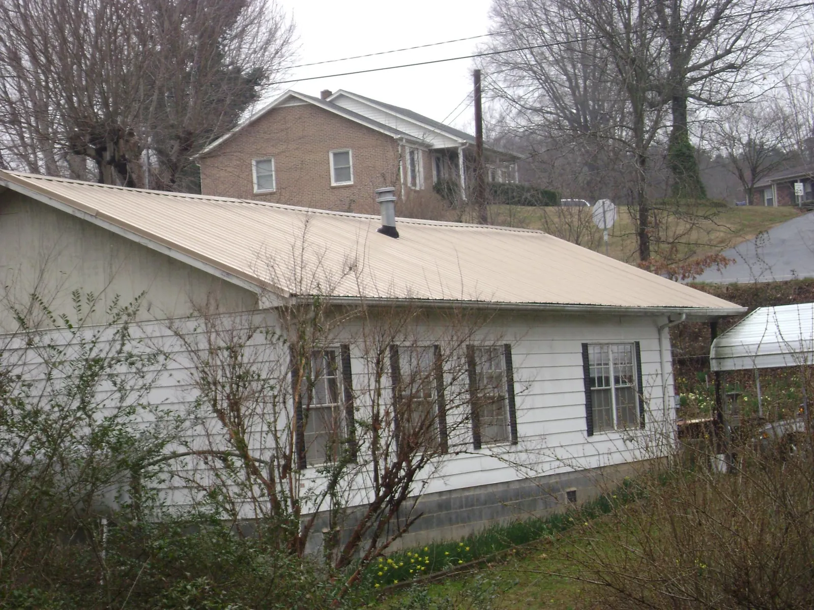 Tan metal roof on a white sided house set into a hillside — Commercial Roofing by Roofing Brothers in West Salisbury